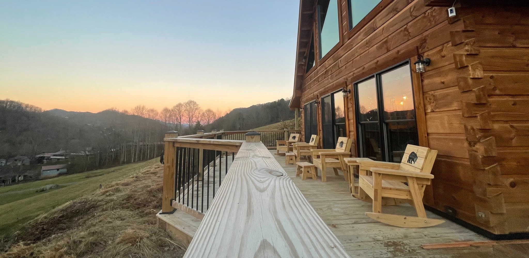 Finished log home with a long pine deck, looking out over the valley at sunset